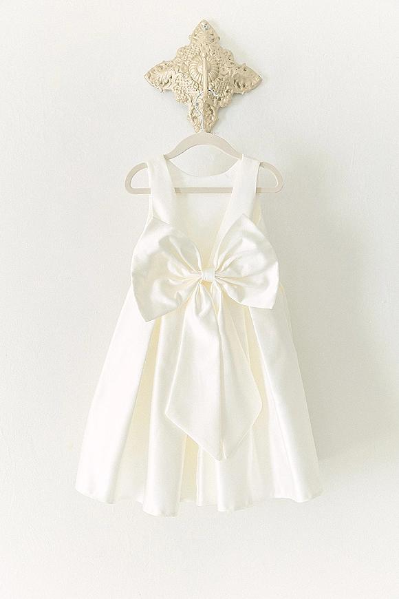 Wedding dress, short wedding dress hanging on a dress hanger with a satin bow on a wall hook against a clean white wall