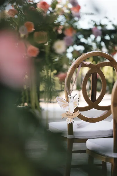 Reserved seating sign hanging as ceremony chair decor, accented with a hummingbird tag, set against garden greenery.