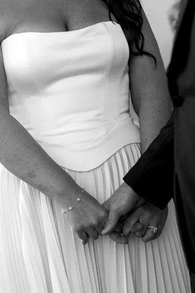 Couple holding hands, her sparkling engagement ring catching light as their fingers intertwine in a tender, timeless wedding moment