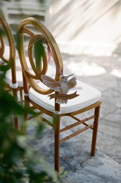 Reserved chair sign serving as ceremony chair signage, featuring a hummingbird motif, on a stone patio with greenery and soft sunlight shadows.