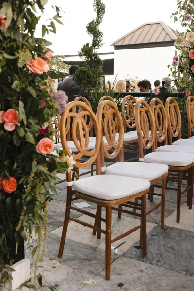Ceremony seating arranged within rooftop ceremony decor, rows of chairs with white cushions facing the aisle on a stone floor under open sky.