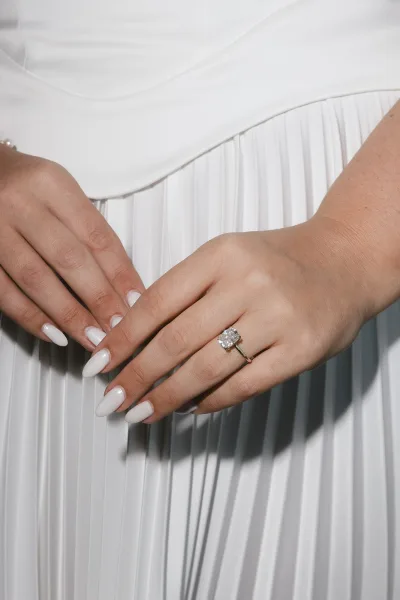 Engagement ring: a solitaire diamond ring on a yellow gold band, shown on manicured bridal hands against pleated wedding dress fabric.