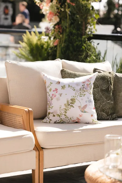 Wedding lounge seating in an outdoor lounge area featuring a cane arm sofa, set against lush garden greenery with a floral installation on the patio.
