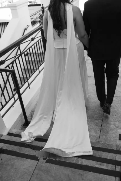 Wedding dress close-up capturing the back of wedding dress with a flowing train as the bride descends a staircase with metal railing.