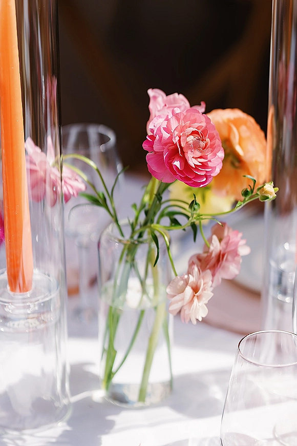 Wedding centerpiece with pink flowers in bud vases, clear glass taper candle holders and greenery on a white tablecloth setting