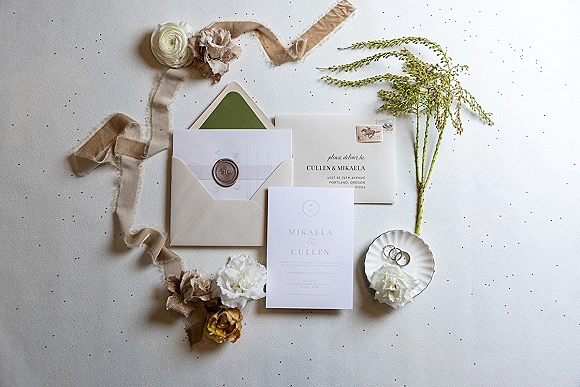 Invitation suite wedding invitation flat lay with wax-sealed envelopes, silk ribbon, flowers and rings on a light tabletop with confetti