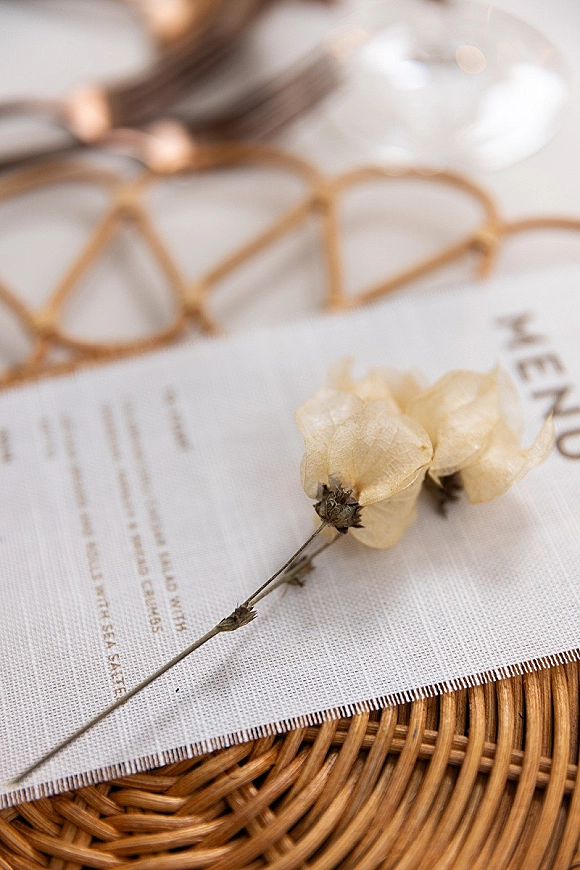 Wedding invitation suite with rustic wedding invitations, dried flower accents, eyeglasses and wine glass on a woven rattan surface