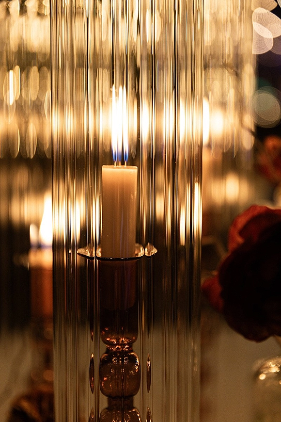 Wedding candle centerpiece with a glass hurricane candle, pillar candle and floral arrangement glowing in moody reception lighting