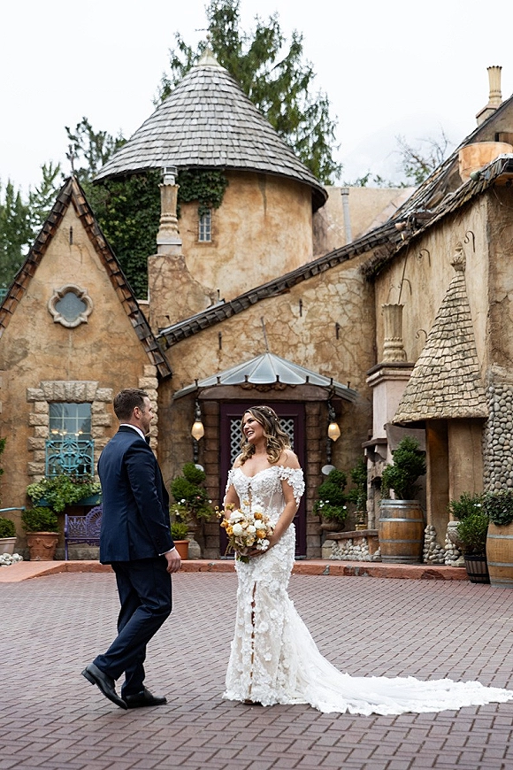 First look moment as bride in lace off-the-shoulder dress with bouquet meets groom in navy suit in ivy brick courtyard by barrels