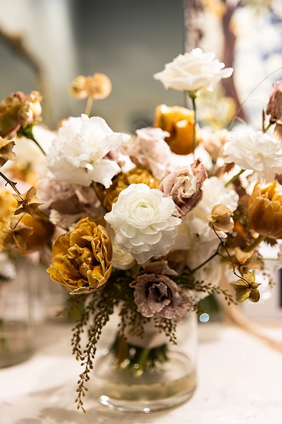Wedding centerpiece with floral centerpiece ideas in a clear glass vase, featuring white and mustard blooms with blush flowers and greenery indoors