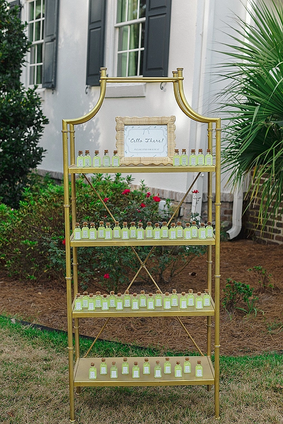 Wedding welcome sign on a gold bar cart with framed sign and mini bottle favors with cork stoppers outside by white wall and shutters