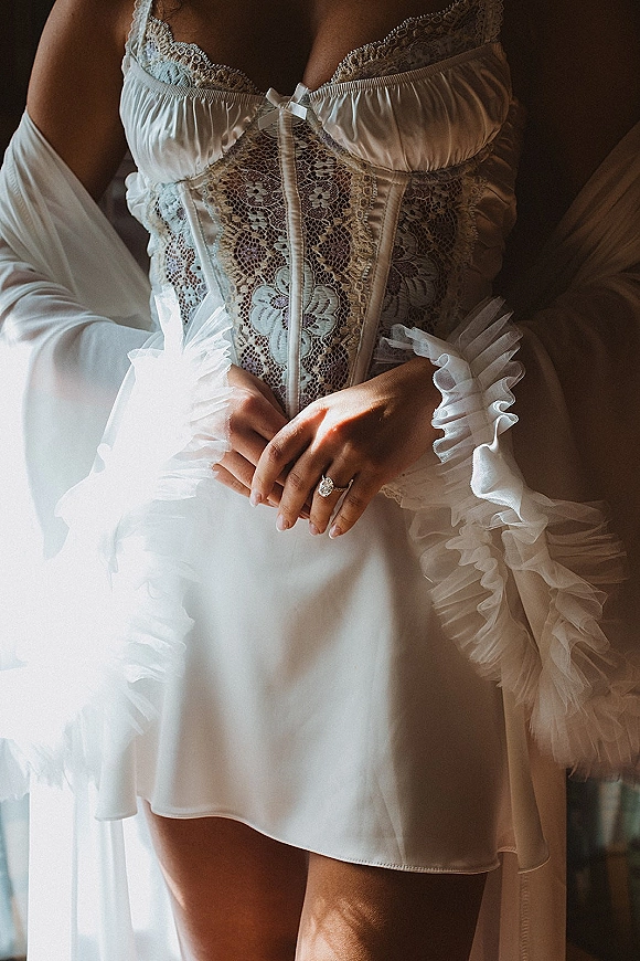 Bridal lingerie with wedding night lingerie details, featuring a white lace corset, satin slip, and sheer robe in soft indoor shadows