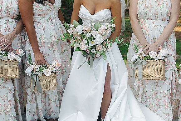 Bridesmaid dresses in floral bridesmaid dresses style as attendants hold wicker baskets with ribboned bouquets amid lush outdoor greenery