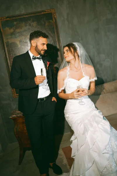 Couple portrait of bride and groom with champagne, leaning close as they toast in an intimate indoor scene