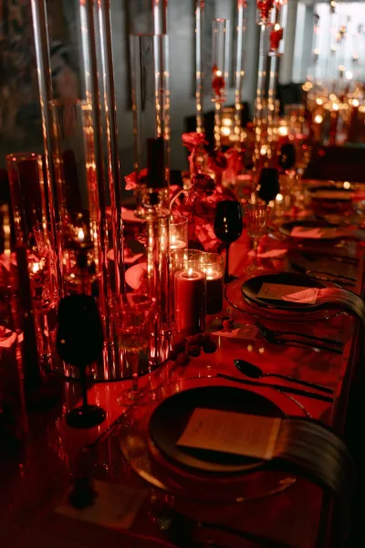 Reception tablescape glowing as a candlelit wedding table with black glassware, set in an indoor venue with a dark wall and ambient lights.