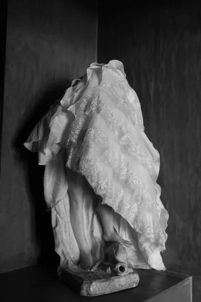 Wedding dress detail of a lace wedding dress styled on a statue, set against a textured wall with a pedestal base.