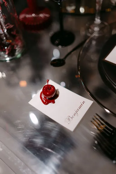 Wedding place card, steadied by a cherry place card holder on a metallic tabletop beside a clear glass vase.