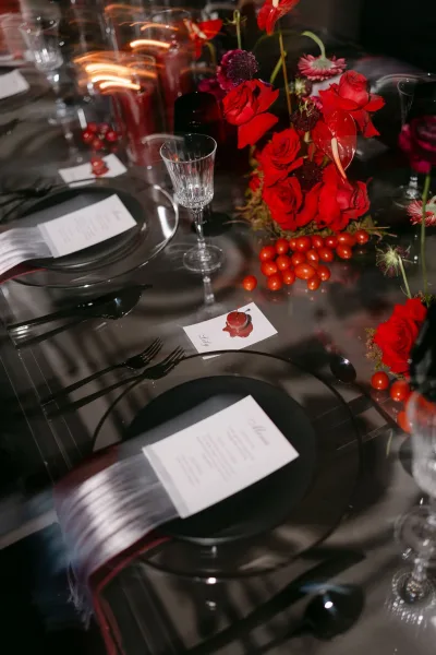 Reception tablescape on a black and red wedding table, accented with red florals on a reflective glass tabletop against a dark background.