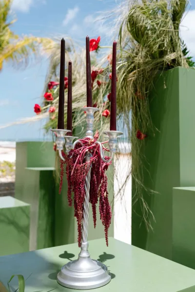 candelabra centerpiece with taper candles crowns wedding candelabra decor on green pedestals amid tropical greenery by a sunny beach