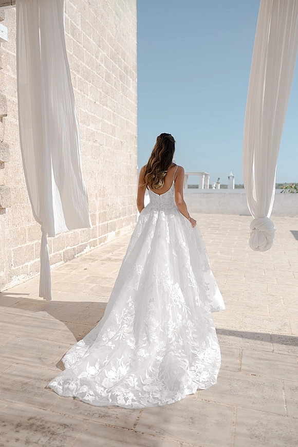 Bridal portrait of a bride from behind in a backless lace wedding dress with a long train, on a terrace patio by a stone wall and blue sky