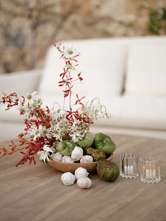 Wedding centerpiece with fruit and vegetable centerpiece styling in a ceramic bowl, wildflowers and red florals with votive candles on a patio table