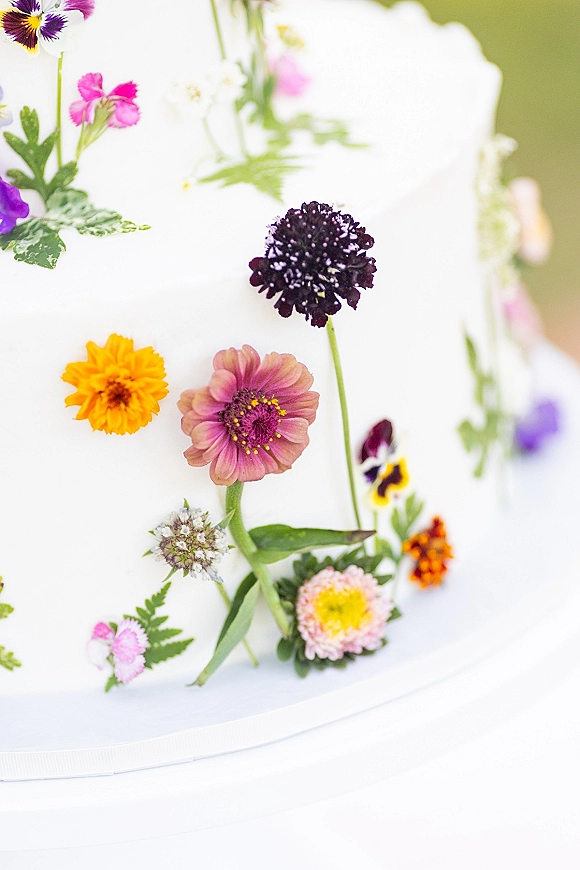 Wedding cake with wildflower wedding cake details, white buttercream frosting topped with fresh flowers against a softly blurred background