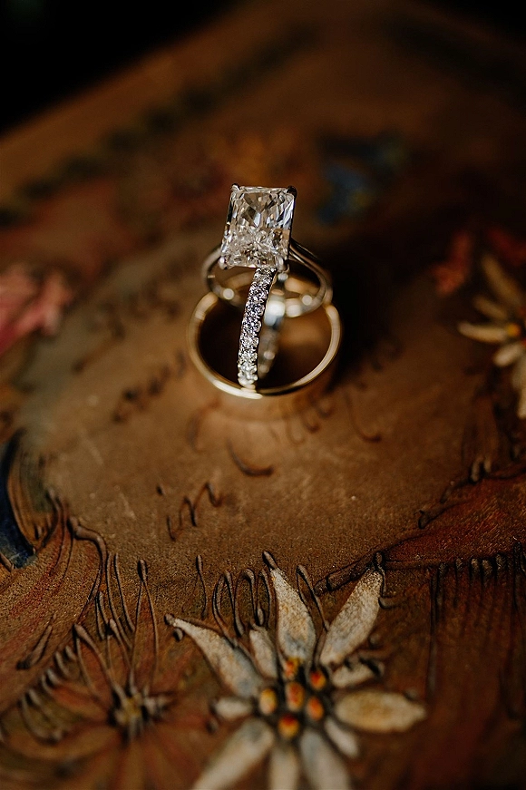 Wedding rings stacked with a diamond engagement ring and pavé band on a vintage floral book cover against a warm brown surface