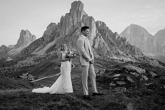 Couple portrait in a black and white wedding portrait style, bride holding bouquet beside groom in light suit on rocky mountain slope