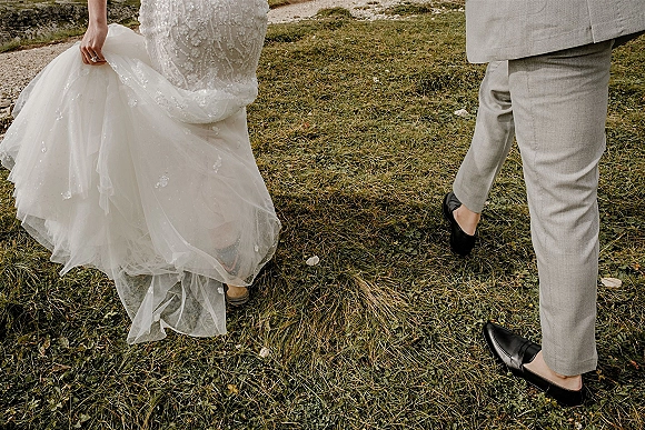 Wedding couple walking away, bride and groom walking away on a gravel path, bride lifting beaded tulle skirt beside groom in light gray suit