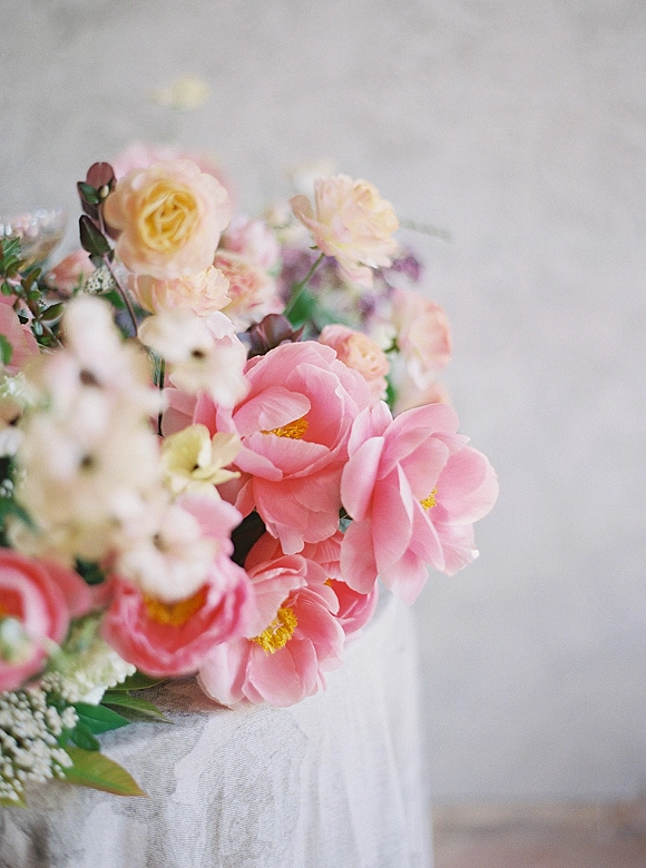 Wedding bouquet with pink peonies and blush roses, lush greenery and white blossoms resting on linen atop a tabletop against a neutral wall
