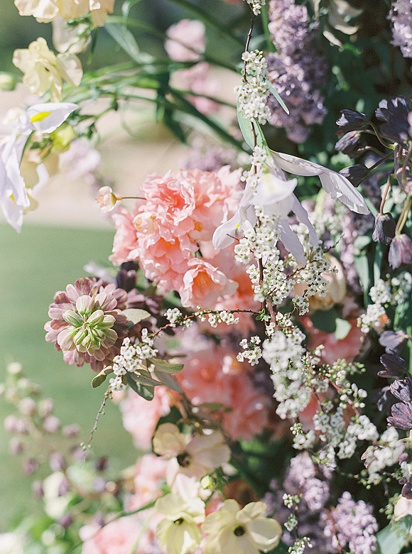 Wedding florals in a ceremony floral arrangement with pink peonies, white orchids, baby's breath, and greenery on a blurred garden lawn backdrop