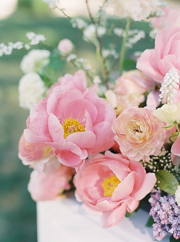 Wedding bouquet with pink peony bouquet blooms, ranunculus and baby's breath, plus lilac and greenery against a soft green blur