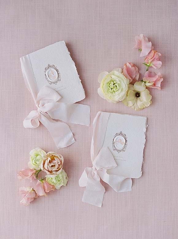 Wedding invitations on handmade paper with deckled edges, blush silk ribbon and wax seal, accented by florals on blush linen backdrop