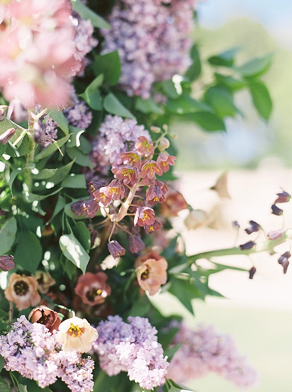 Wedding floral arrangement with lilac wedding flowers and pink blooms, framed by lush greenery in soft sunlight outdoors