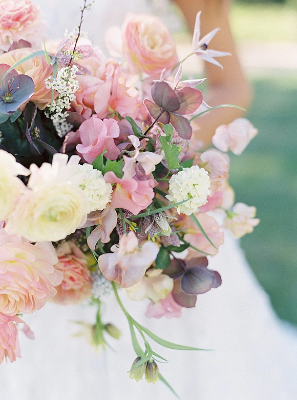 Bridal bouquet of pastel wedding bouquet blooms with ranunculus, sweet peas, hydrangea and eucalyptus against soft outdoor greenery bokeh