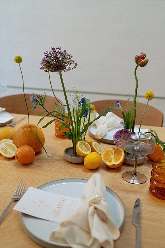 Reception tablescape wedding table decor with wildflower centerpieces, citrus fruit, ribbed glass goblets, and amber vases on a wood table