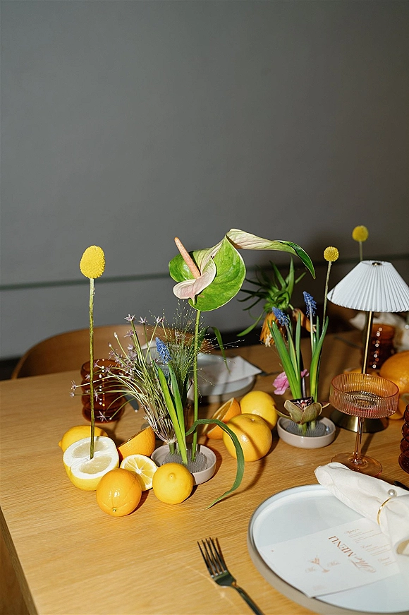 Reception tablescape with citrus wedding tablescape accents, lemons and anthurium bud vases, place cards, candles and ribbed goblets on wood table