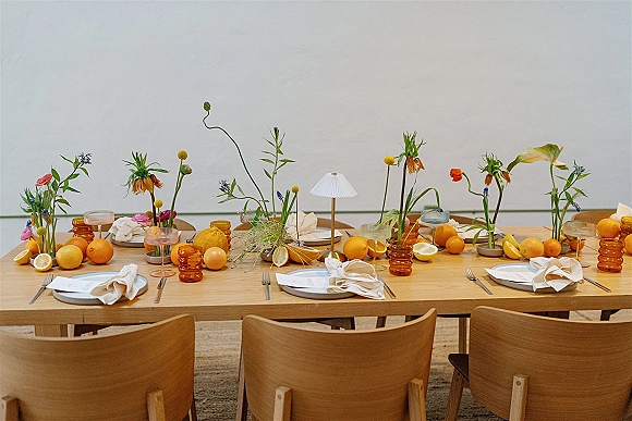 Reception tablescape with modern wedding tablescape styling on a wood table, linen napkins, amber tumblers, wildflowers, and citrus fruit centerpiece