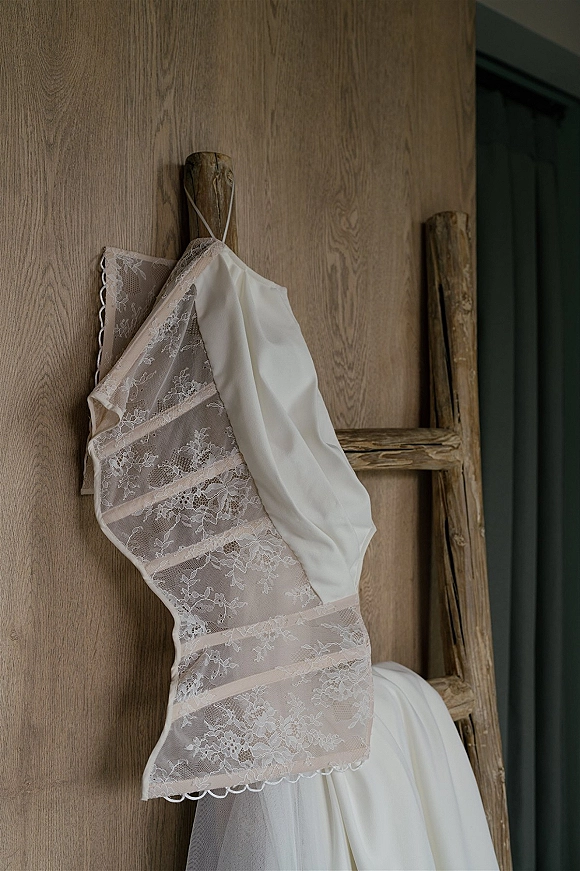 Wedding dress with lace wedding dress bodice, spaghetti straps and tulle skirt hanging on a rustic wooden ladder by a doorway