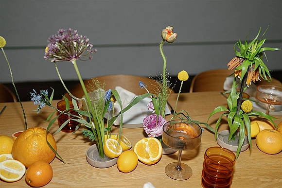Reception tablescape with wildflower wedding centerpieces, citrus fruit, amber glassware, coupe glasses, and taper candles on a wood table