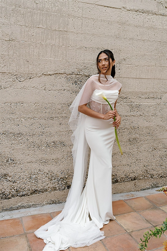 Bridal portrait of a modern bridal portrait bride in a strapless wedding dress holding a white calla lily before a textured concrete wall