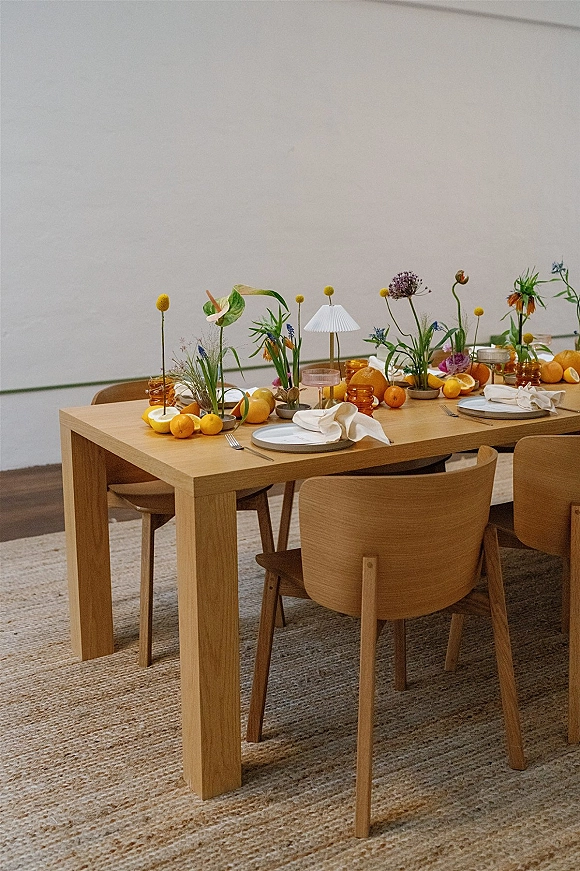 Reception tablescape with modern wedding tablescape styling, citrus slices, bud vases, amber glassware, and a table lamp on a wood table