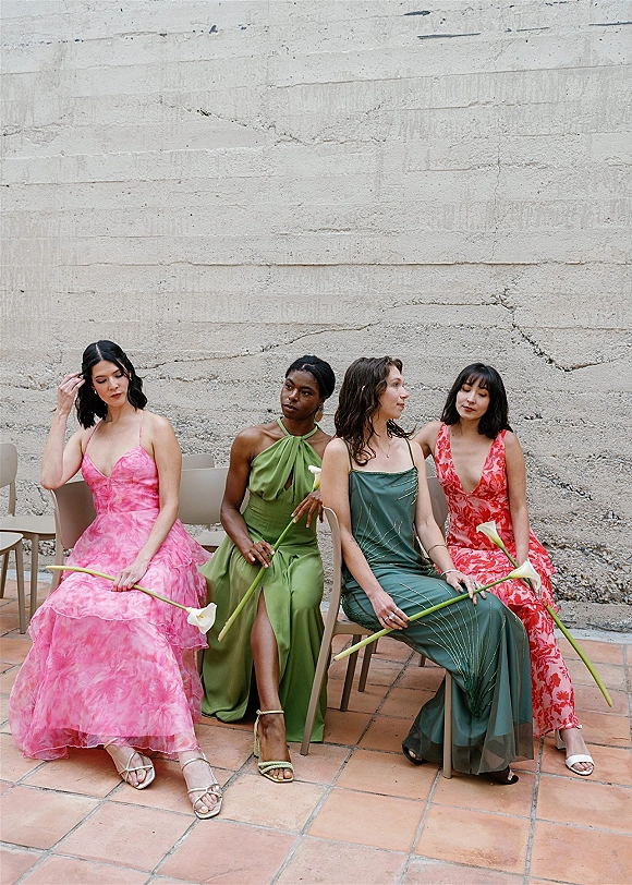 Bridesmaid dresses in mismatched styles as seated bridesmaids hold calla lilies, with strappy heels by chairs on terracotta tiles