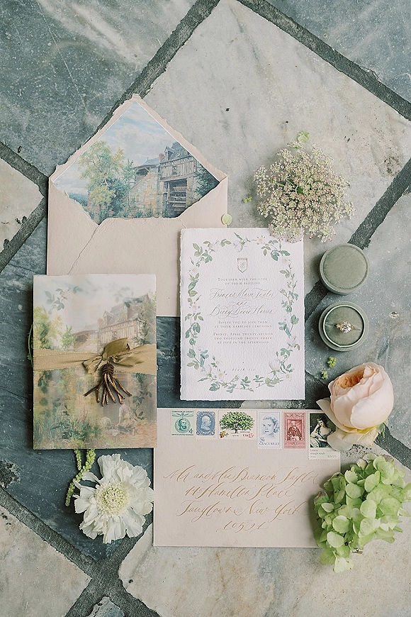 Wedding invitation suite with watercolor wedding invitations, wax-sealed envelopes, ribbon, stamps, and ring on a marble tile floor