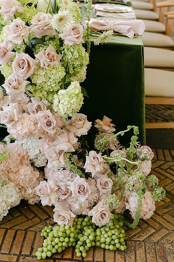 Wedding floral installation with a blush rose installation of hydrangeas and green amaranthus beside a velvet tablescape with pearl rings and grapes