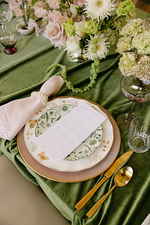 Reception tablescape with green wedding tablescape details, layered plates, printed menu, pearl napkin ring, and gold flatware beside glassware