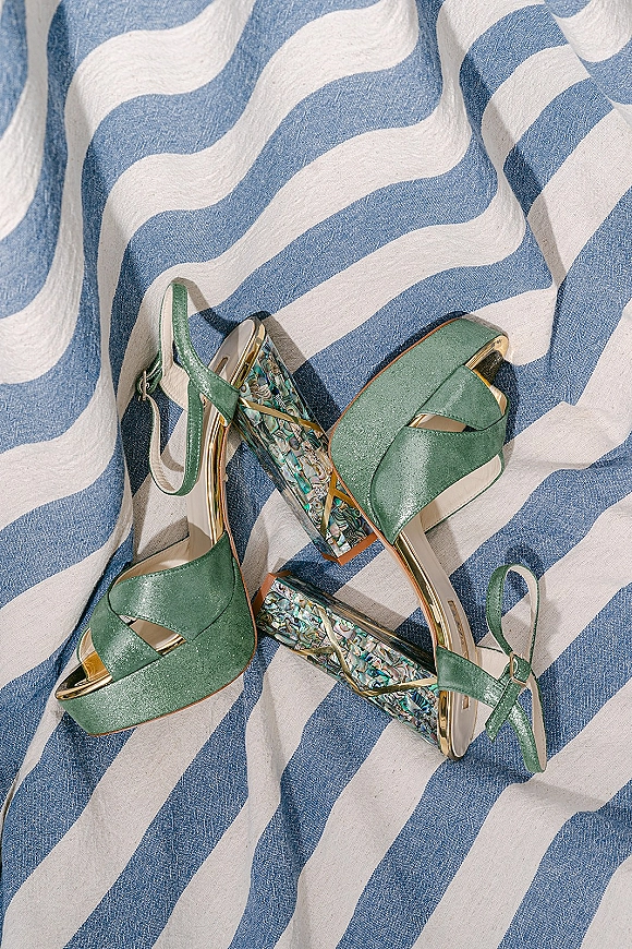 Wedding shoes in green bridal shoes style with ankle straps, platform soles, and iridescent block heels on blue-and-white wavy fabric