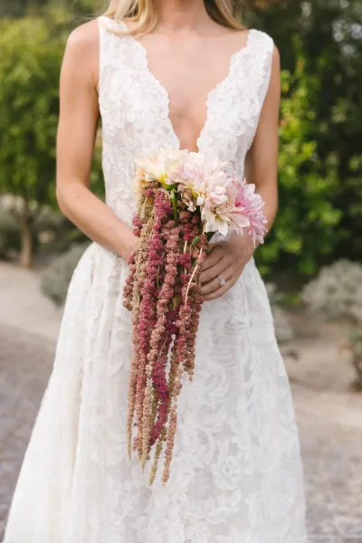 Bridal bouquet with cascading wedding bouquet shape, dahlias and hanging amaranthus over a lace deep V dress on a garden pathway