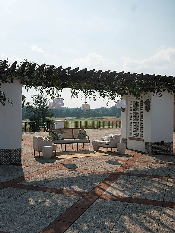 Outdoor lounge setup with wedding cocktail hour lounge seating under a pergola, greenery garland and string lights on a tiled courtyard terrace