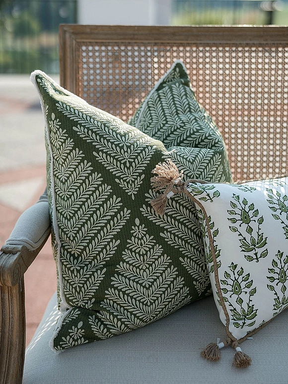Lounge chair styling with outdoor lounge seating, layered green and patterned throw pillows with tassels on a cane-back chair on a patio